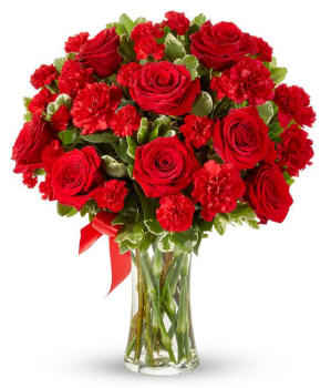 Floral arrangement featuring red roses, red carnations, red mini carnations, and a decorative red ribbon, florist delivered in a clear glass vase.