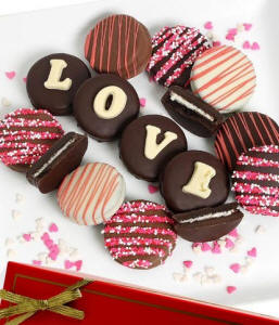 Chocolate-covered Oreo cookies spelling 'LOVE' with assorted rainbow-striped, drizzled cookies on a white serving tray
