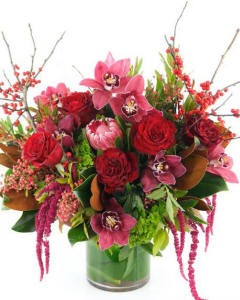 WINTER EXTRAVAGANZA-This lush design features the warm and rich colors of the season with luxurious red roses and winter textures made extra special by the addition of tropical orchid blooms, exotic protea, and hanging amaranthuS.- ARRANGEMENTS